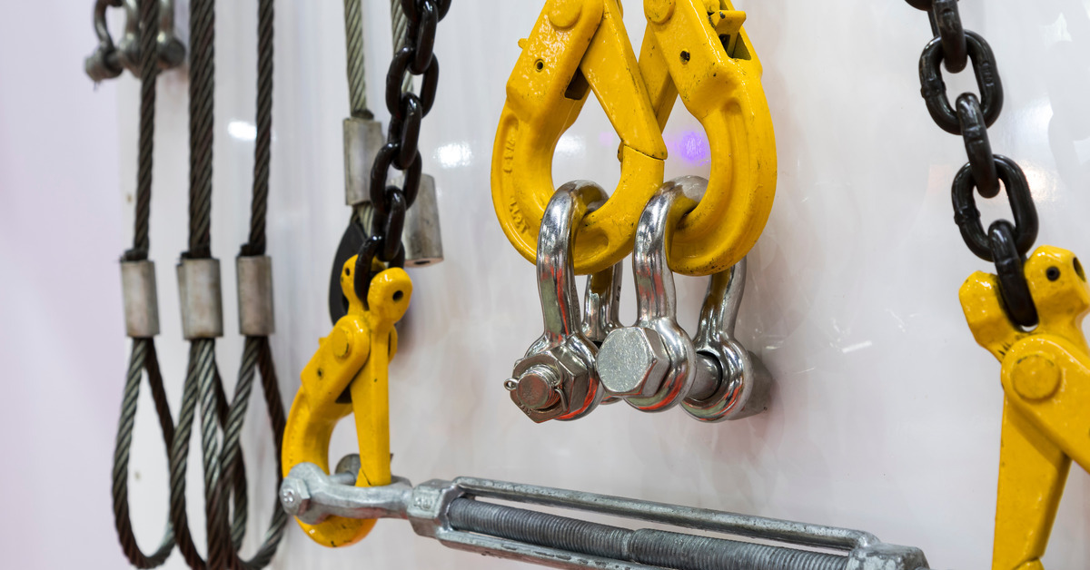 Various industrial crane components hanging from a white wall, including hooks, chains, and steel wires.