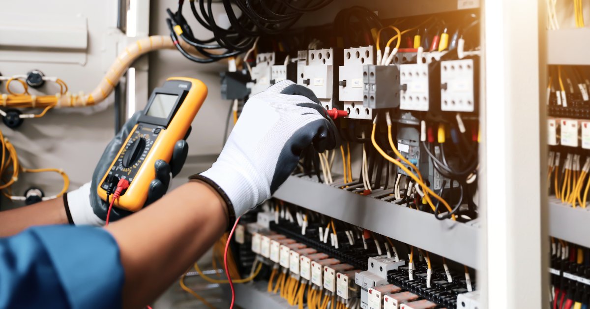 A close-up of an engineer's hands testing the electrical current voltage of a circuit breaker terminal.