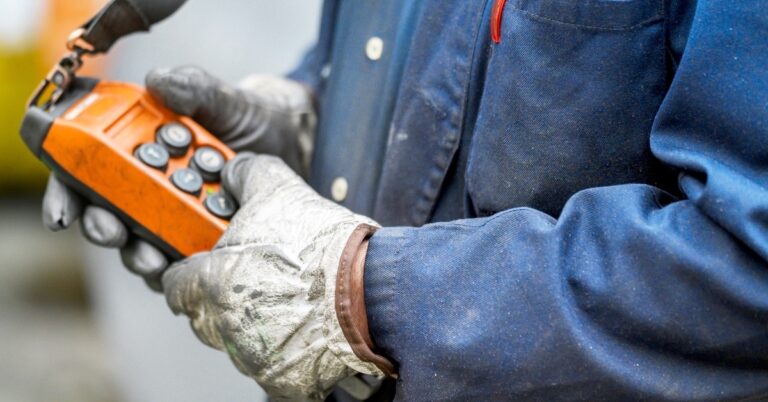 A close-up of a worker with a blue shirt and white gloves pressing the buttons of a crane pendant control station.