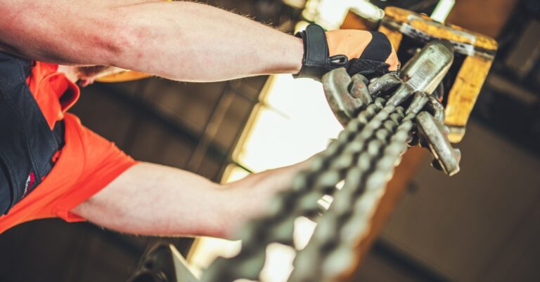 A man wearing a safety vest and hard hat adjusting the chains of an overhead crane lift, viewed from below.