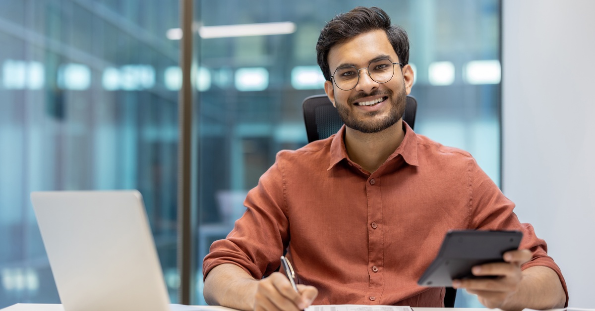 A professional electrical engineer using a calculator and a laptop for fuse selection calculations in a modern office setting