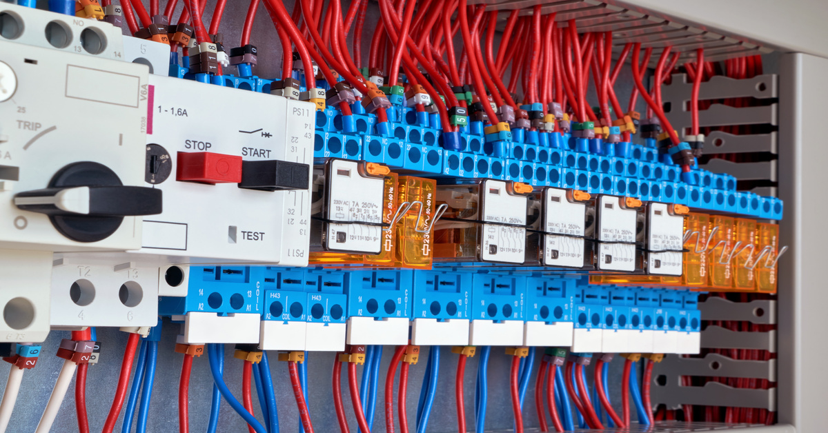 Electrical relays and circuit breakers with blue terminals and red wiring in an industrial control panel installation.