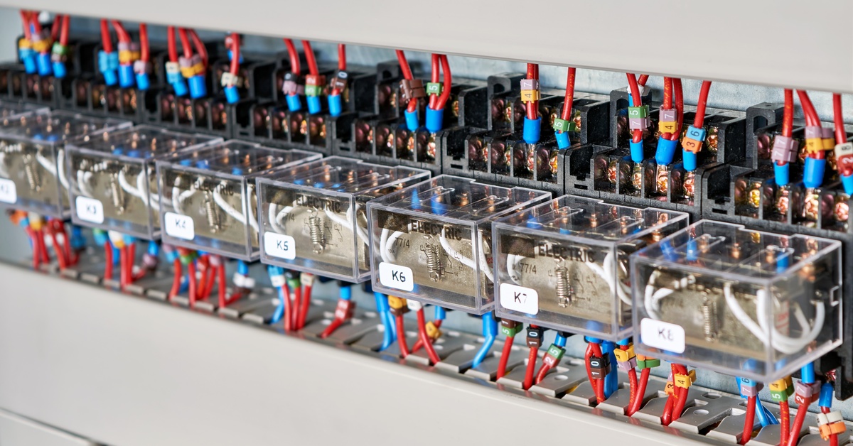 An electrical control panel with multiple transparent electrical relays and color-coded wiring connections mounted in a row.