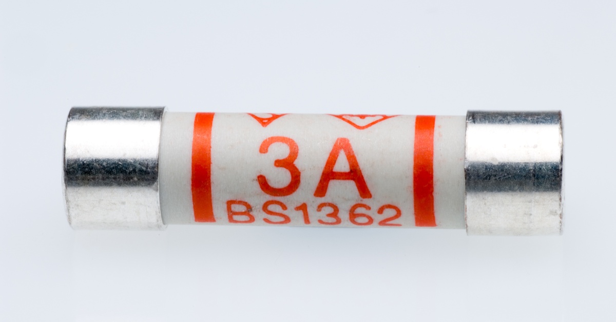 A white ceramic time delay fuse with silver end caps and a red 3A BS1362 rating label against a white background.